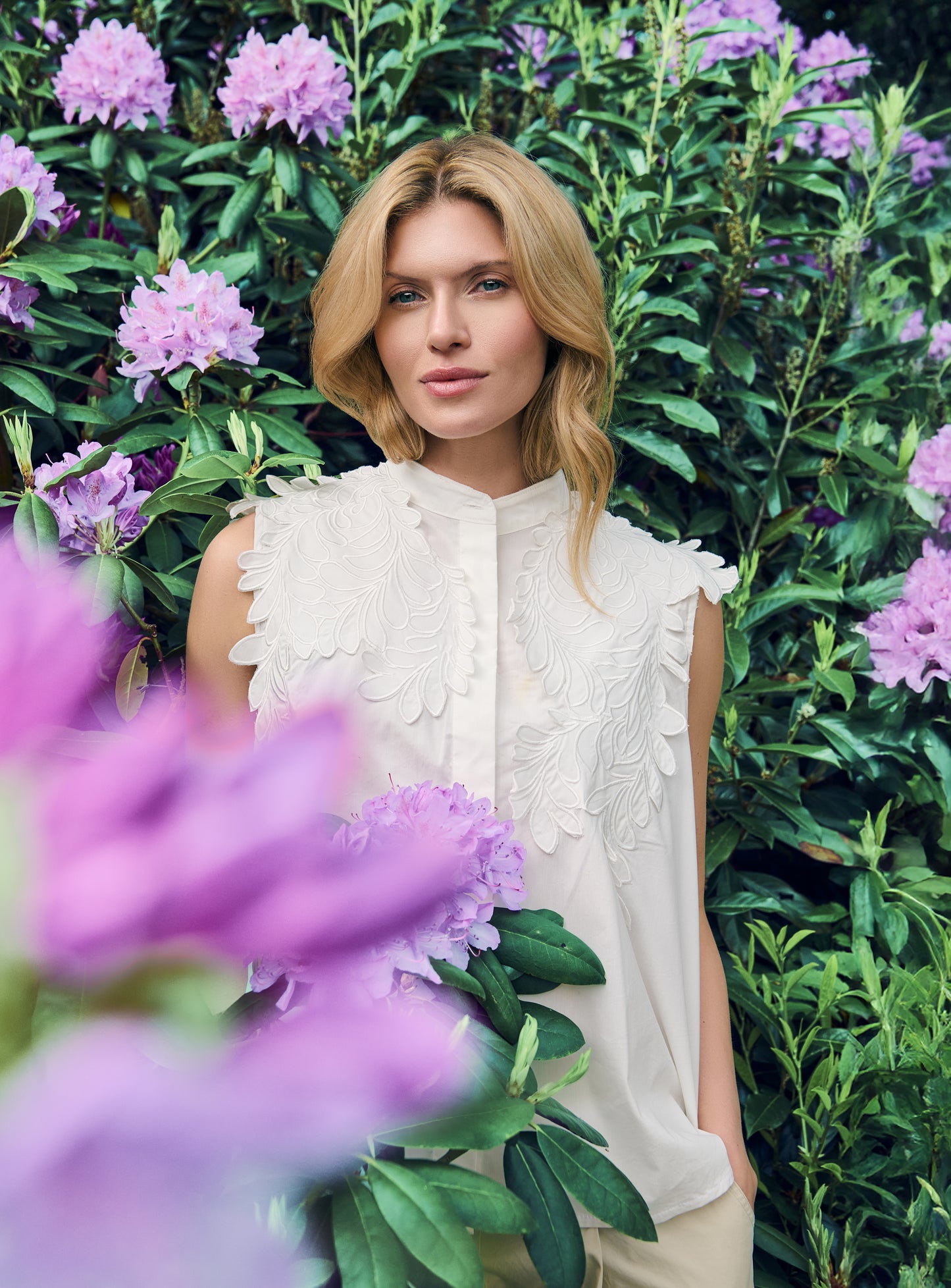 Lilac sleeveless blouse with a band collar and concealed buttons, featuring intricate tonal floral embroidery layered across the shoulders and upper front.