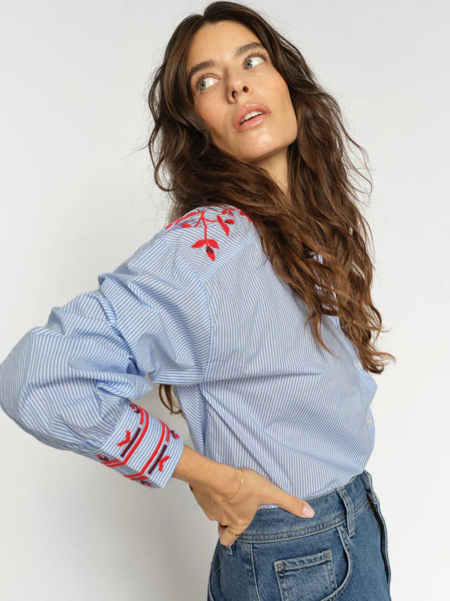 Woman wearing a blue striped shirt with red embroidery on a white background
