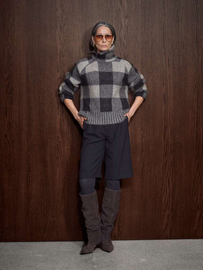 Person wearing a checkered sweater and knee-high boots against a wooden wall.