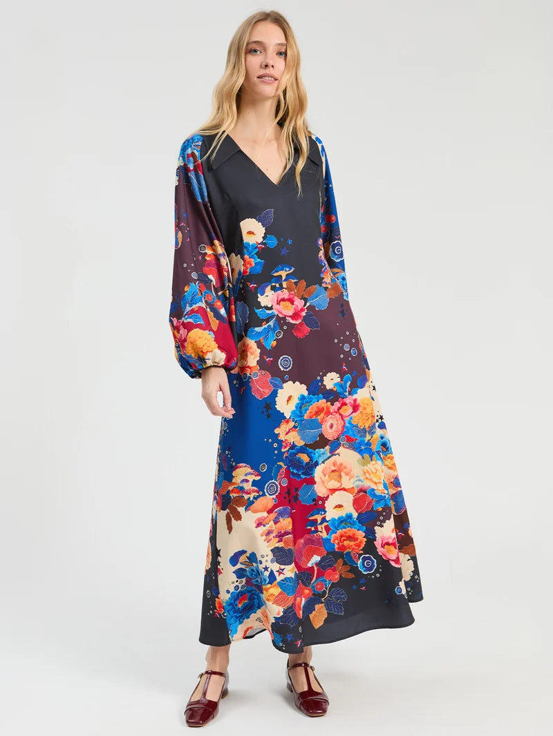 A woman modeling a long-sleeved maxi dress with a dark charcoal base and a vibrant multicolor floral print. Perfect for weddings, birthdays 