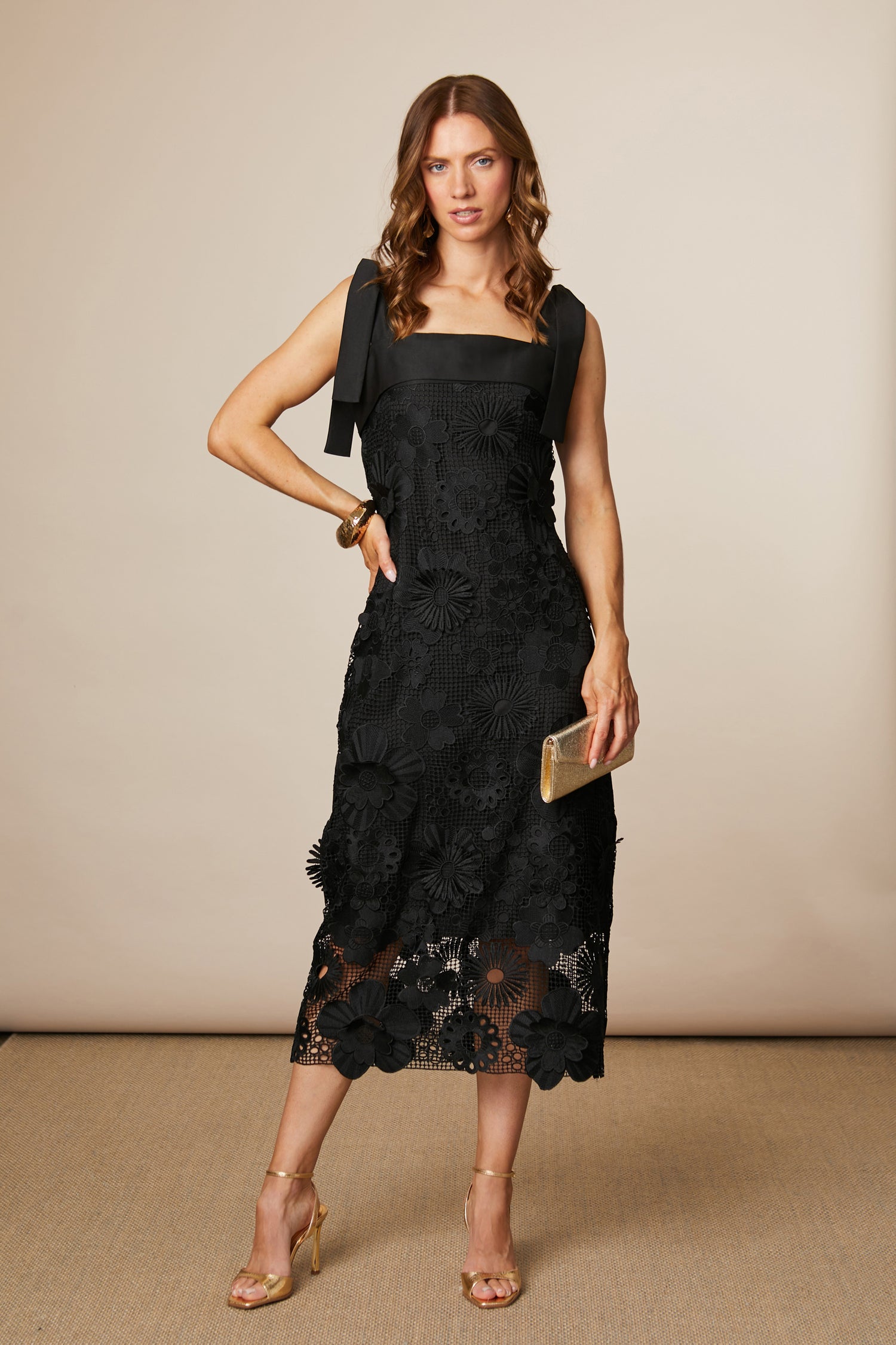 Woman wearing a black lace dress holding a clutch against a beige background