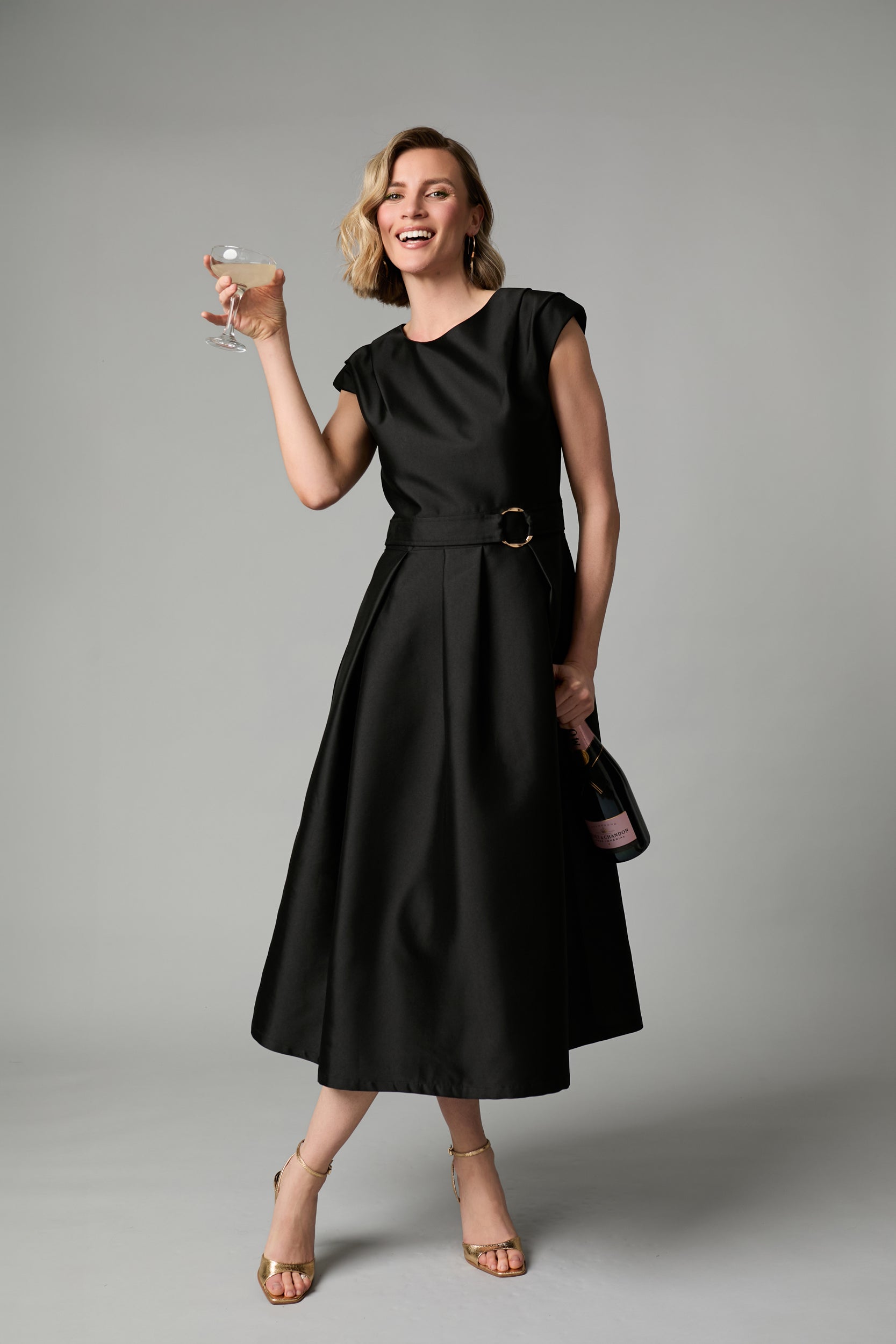 A woman modeling a Fee G black midi dress with a cinched waist and gold buckle belt. perfect for any occasion 