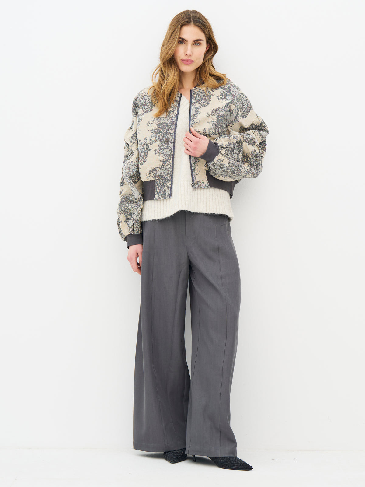 A woman modeling a cropped beige and gray floral patterned jacket with dark gray ribbed trim, from Nu Denmark