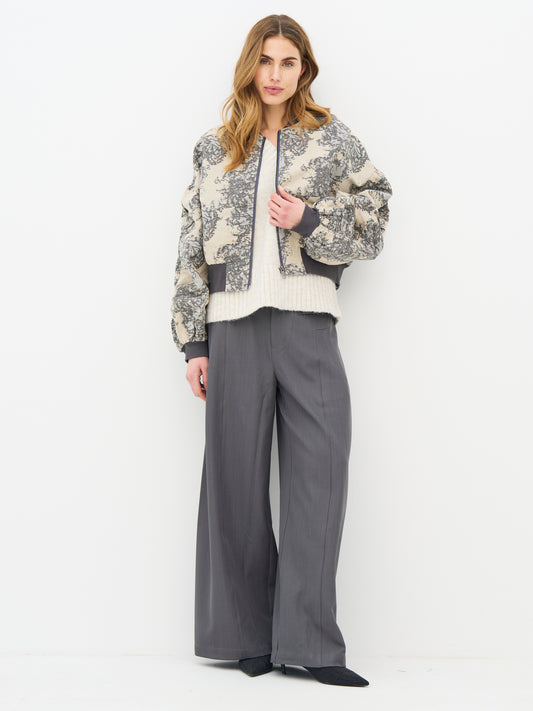 A woman modeling a cropped beige and gray floral patterned jacket with dark gray ribbed trim, from Nu Denmark