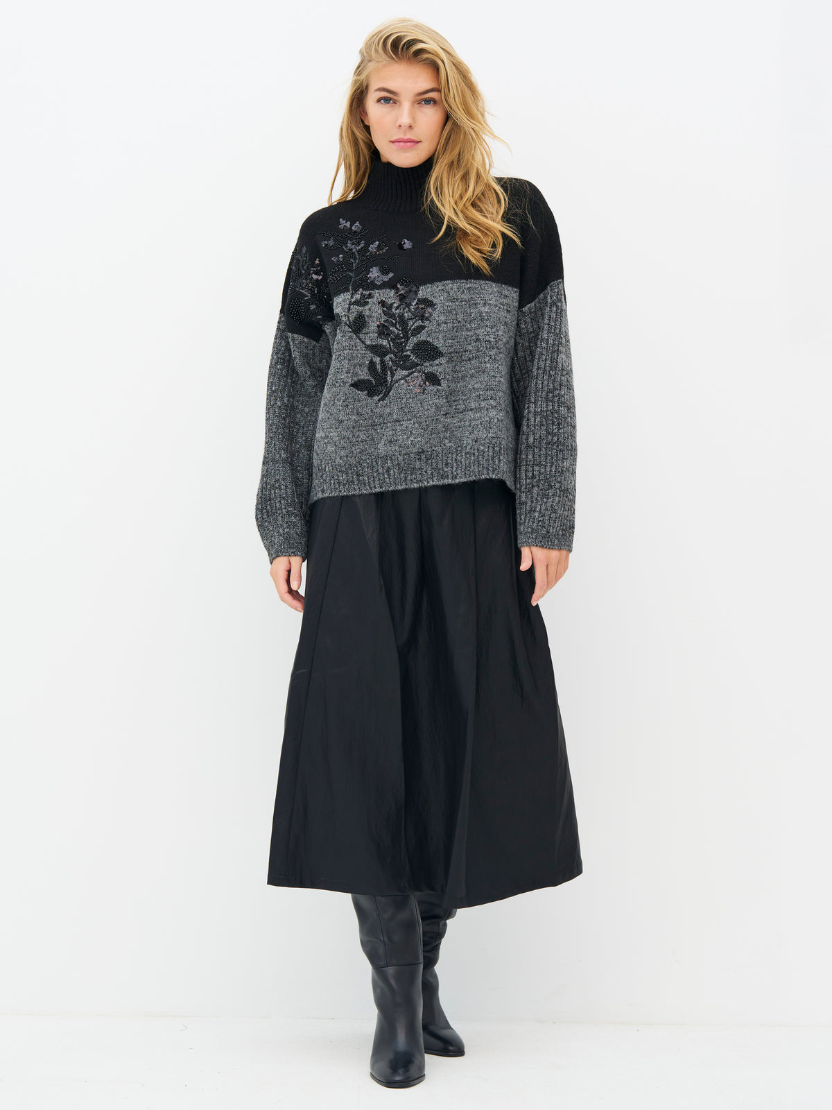A woman modeling a black and gray knit turtleneck sweater with a floral pattern on the front, Nu denmark