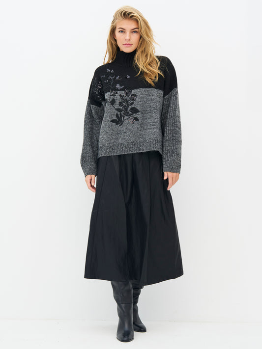 A woman modeling a black and gray knit turtleneck sweater with a floral pattern on the front, Nu denmark