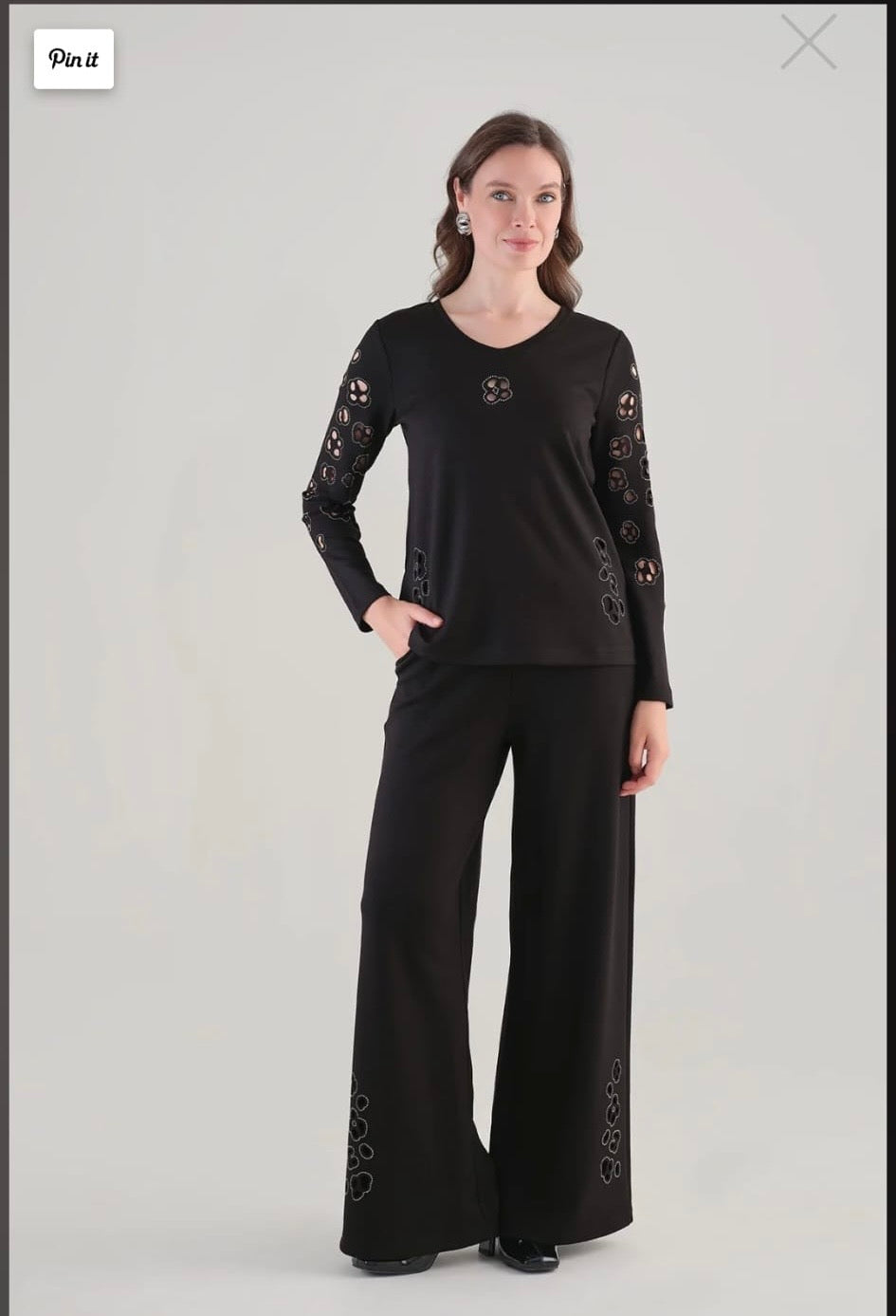 A woman modeling a black long-sleeve top and matching wide-leg pants. The outfit features lace-up detailing on the sleeves and lower legs.