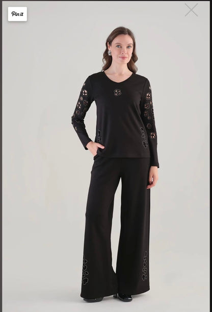 A woman modeling a black long-sleeve top and matching wide-leg pants. The outfit features lace-up detailing on the sleeves and lower legs.