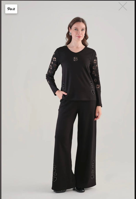 A woman modeling a black long-sleeve top and matching wide-leg pants. The outfit features lace-up detailing on the sleeves and lower legs.