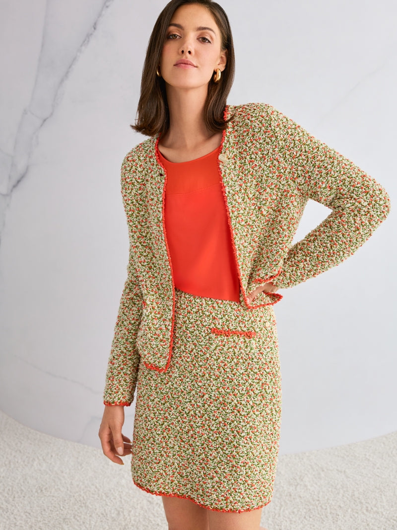 Woman wearing a knitted jacket and  with an orange top against a light background