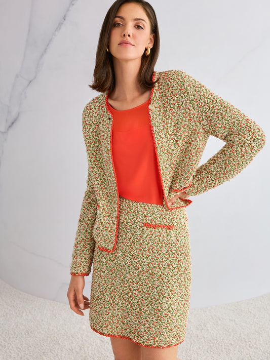 Woman wearing a knitted jacket and  with an orange top against a light background