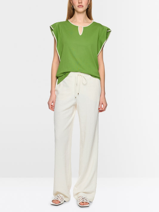 Woman wearing a green top and white pants on a white background