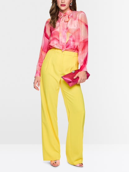 Woman wearing a pink blouse and yellow pants with a white background