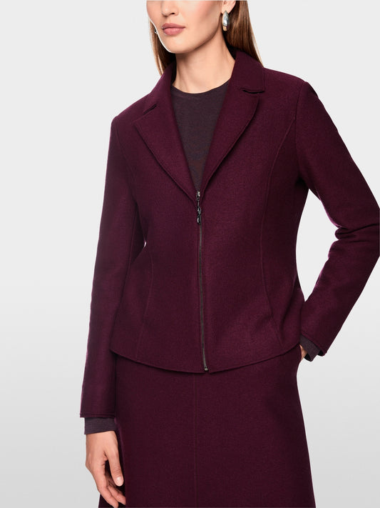 A woman wearing a structured, deep burgundy zip-front jacket with notched lapels and a matching skirt, photographed against a clean light gray studio background.