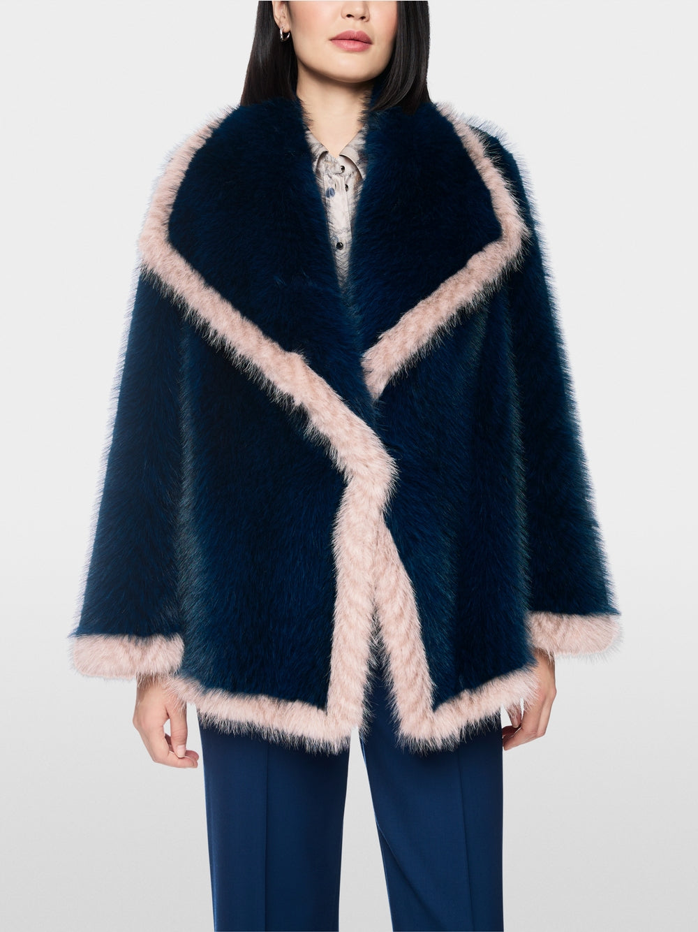 A model wearing a dark navy blue faux fur wrap jacket with light pink trim, paired with navy trousers, against a plain light gray background.