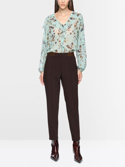 A model wearing a light green floral long-sleeve blouse tucked into dark brown trousers, paired with dark brown pointed-toe ankle boots, against a plain light gray studio background.