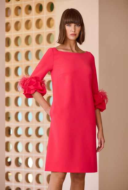 Model wearing a bright pink shift dress with boat neckline and feather trim three-quarter sleeves, styled for a modern occasion look