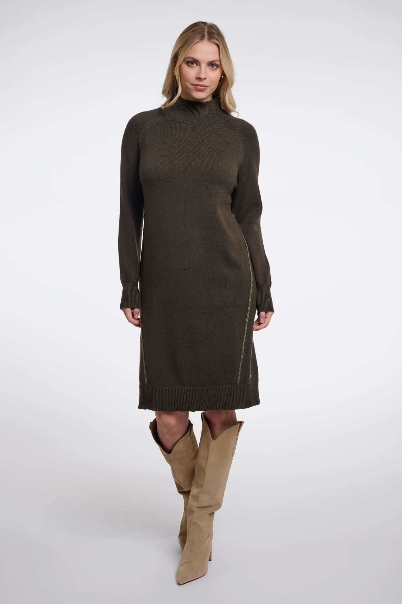 A woman modeling a dark olive green mock-neck knit sweater dress with side zip details, paired with tan knee-high boots, against a light gray studio background.