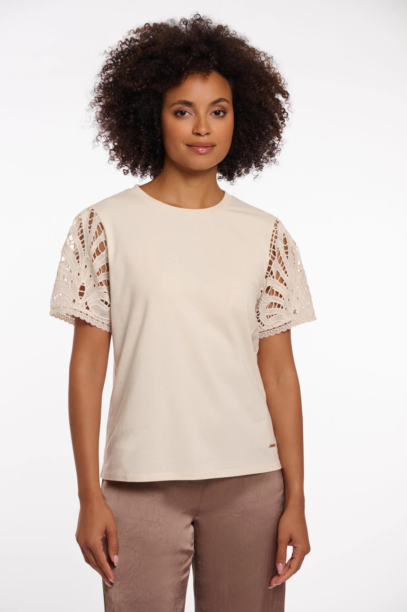Woman wearing a beige top with lace sleeves on a white background