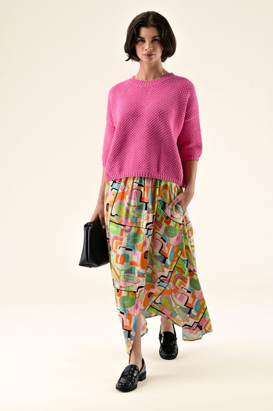 Woman wearing a pink sweater and colorful patterned skirt on a white background