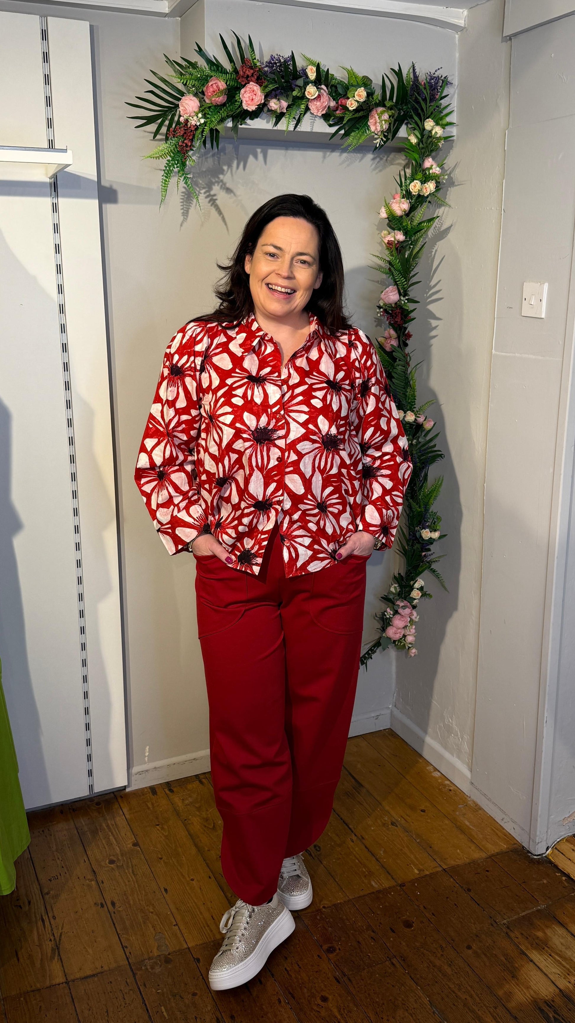 Woman in a red outfit with a floral pattern standing in a room with decorative flowers on the wall.