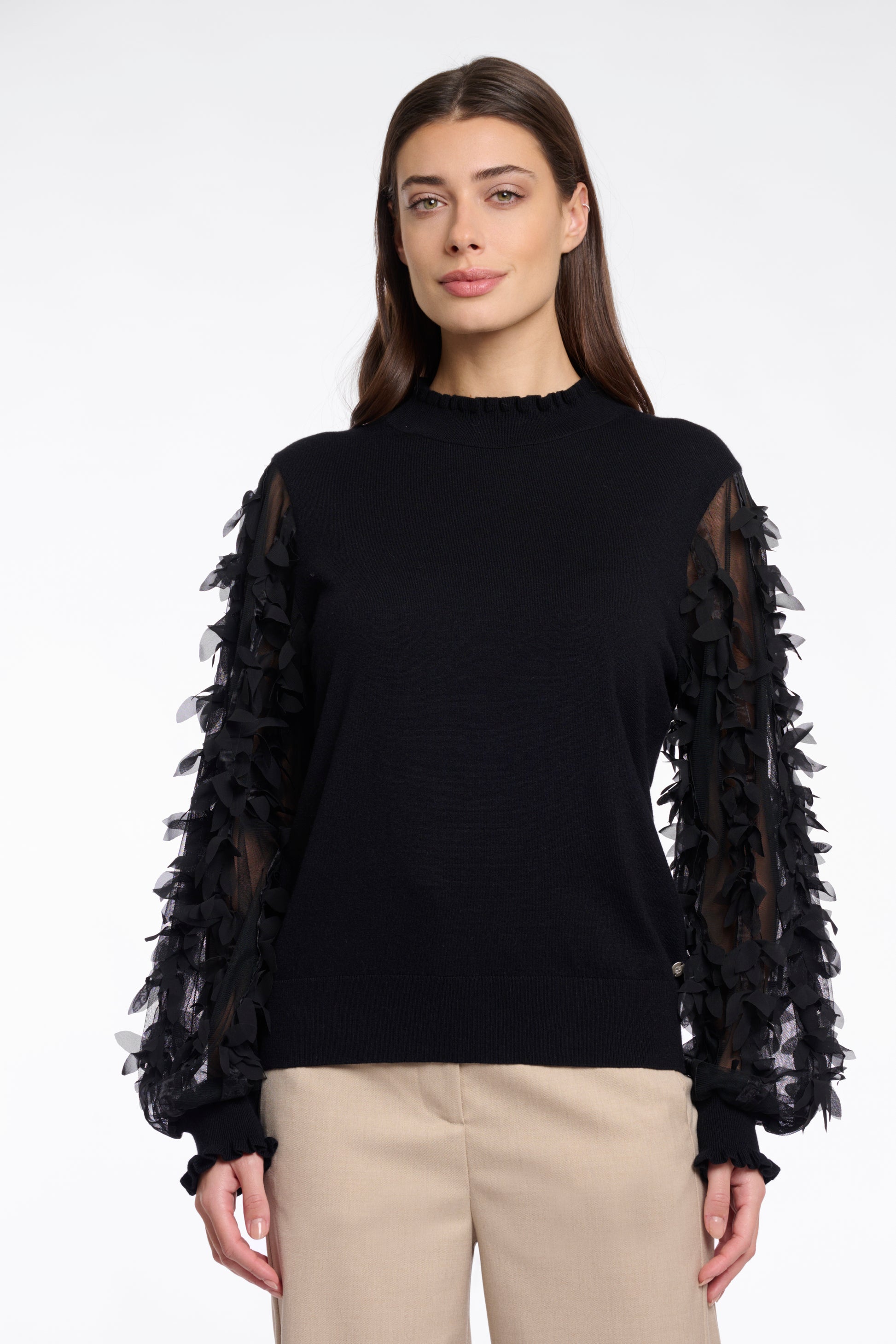 Woman wearing a black sweater with sheer sleeves featuring floral patterns on a white background