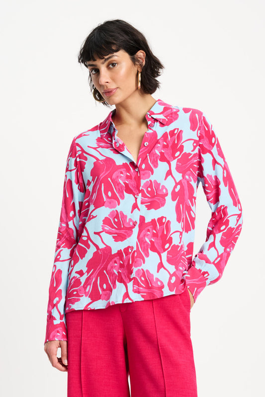 Woman wearing a pink and white floral blouse with pink pants on a white background