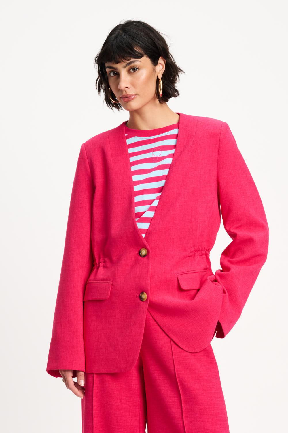 Woman wearing a bright pink suit with a striped shirt on a white background