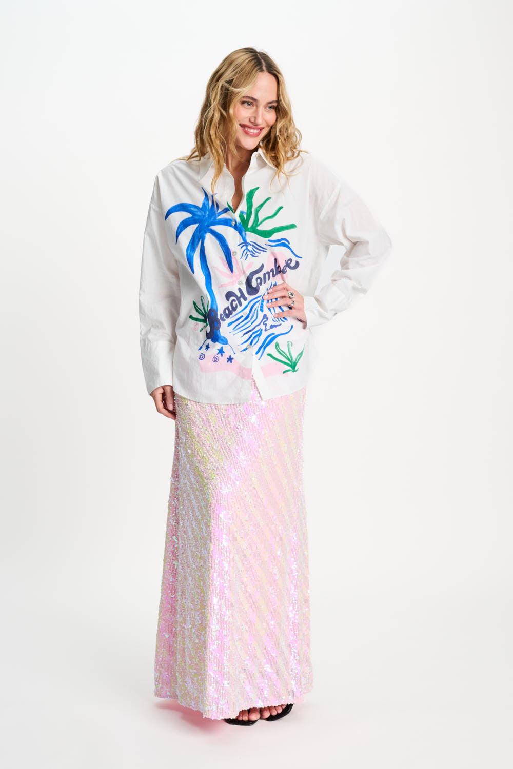 Woman wearing a white shirt with colorful palm tree design and a pink skirt on a white background
