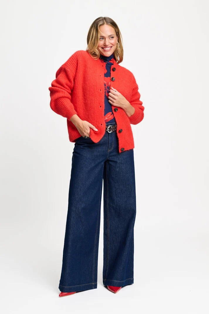 A woman modeling a bright red knit cardigan with balloon sleeves, worn over a navy top 