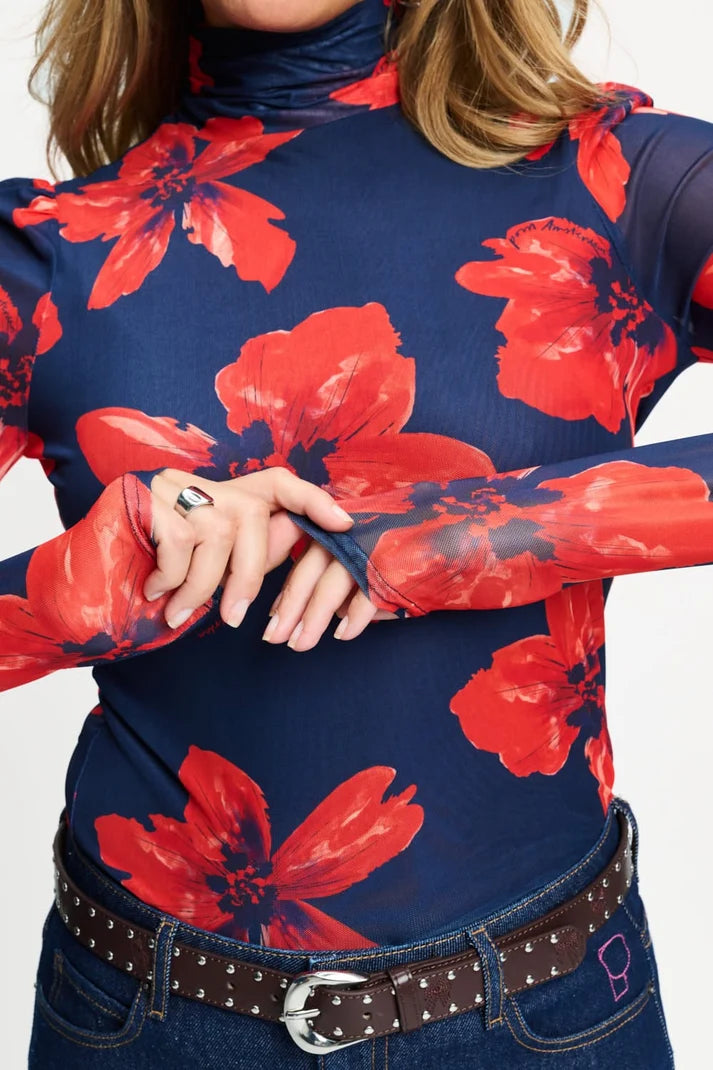 A close-up of a model wearing a navy blue mock-neck long-sleeve top with a vibrant red floral print,